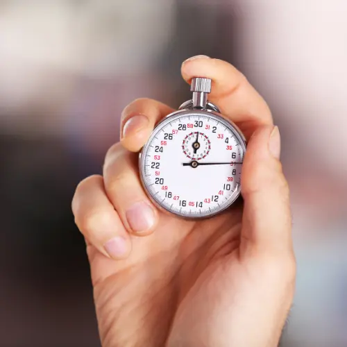 Ein elektronisches Zeiterfassungsterminal, daneben ein Mitarbeiter, der seine Arbeitszeit stempelt, während im Hintergrund ein Betriebsrat die Umsetzung der Arbeitszeiterfassung überwacht.