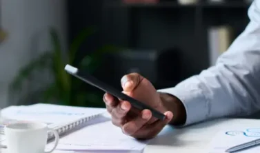 Mitarbeiter hält Smartphone in der Hand und postet auf LinkedIn – im Hintergrund das Büro, symbolisch für die Notwendigkeit einer Betriebsvereinbarung Social Media im Unternehmen