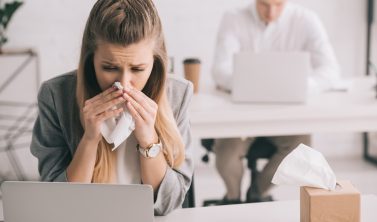 Ein überlasteter Mitarbeiter im Büro dokumentiert bei einer herbstlichen Krankheitswelle die Überstunden und die Krankheitsvertretung Arbeitszeit.