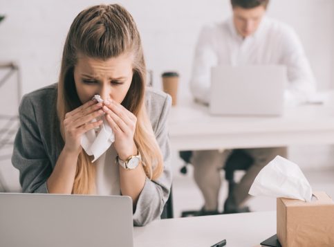 Ein überlasteter Mitarbeiter im Büro dokumentiert bei einer herbstlichen Krankheitswelle die Überstunden und die Krankheitsvertretung Arbeitszeit.