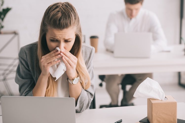 Ein überlasteter Mitarbeiter im Büro dokumentiert bei einer herbstlichen Krankheitswelle die Überstunden und die Krankheitsvertretung Arbeitszeit.